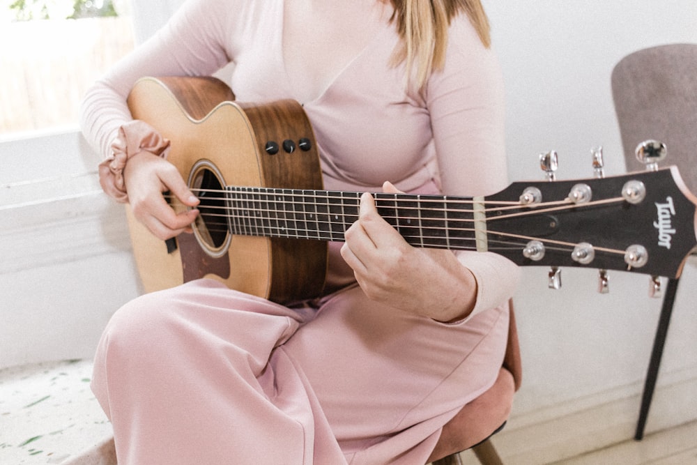 woman in pink long sleeve shirt playing brown acoustic guitar