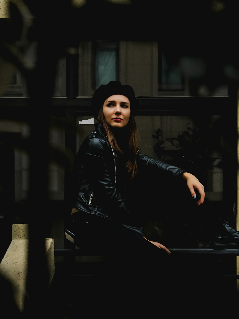 woman in black leather jacket and black knit cap sitting on brown wooden bench