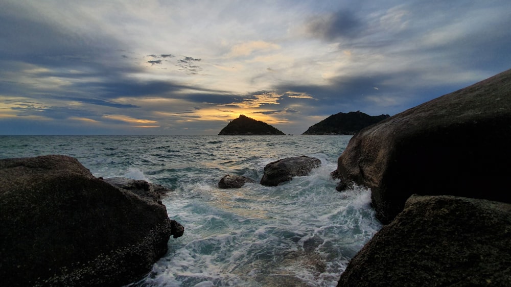 rocky shore under cloudy sky during sunset