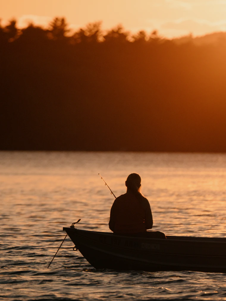 A lone angler silhouetted on a boat as the sun sets over open water