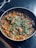A pan filled with a rich, red-orange curry containing chunks of vegetables or meat, topped with fresh green cilantro leaves. The dish appears freshly cooked and is placed on a dark countertop surface.