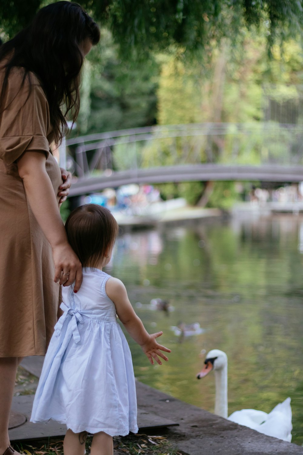girl in white dress standing beside girl in brown dress near body of water during daytime
