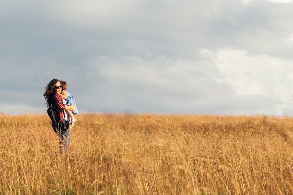 woman in blue jacket walking on brown grass field during daytime