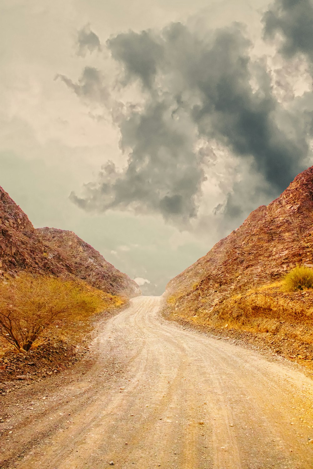 brown dirt road between brown mountains under white clouds during daytime