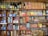 A vintage display of various retro packaging and bottles is arranged on wooden shelves. The shelves are filled with colorful boxes and cans of different food products, cleaning items, and glass bottles with old-style labels. The collection includes brands and labels primarily in French.