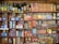 A vintage display of various retro packaging and bottles is arranged on wooden shelves. The shelves are filled with colorful boxes and cans of different food products, cleaning items, and glass bottles with old-style labels. The collection includes brands and labels primarily in French.