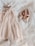 A delicate, cream-colored tulle dress paired with matching metallic pink ballet shoes. The soft textures and gentle hues create an elegant and serene atmosphere. The items rest on layered tulle fabric, enhancing the overall softness and femininity of the composition.