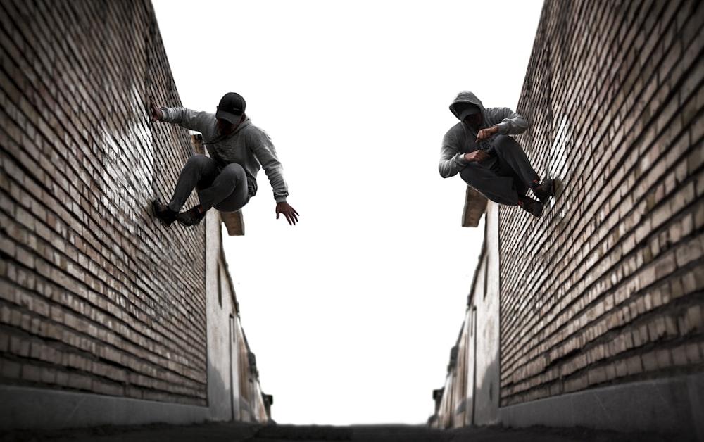 Homme en veste noire et pantalon noir assis sur un mur de béton brun pendant la journée