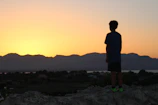 A silhouette of a man standing on a cliff at dusk, looking out over a vast, darkening landscape.