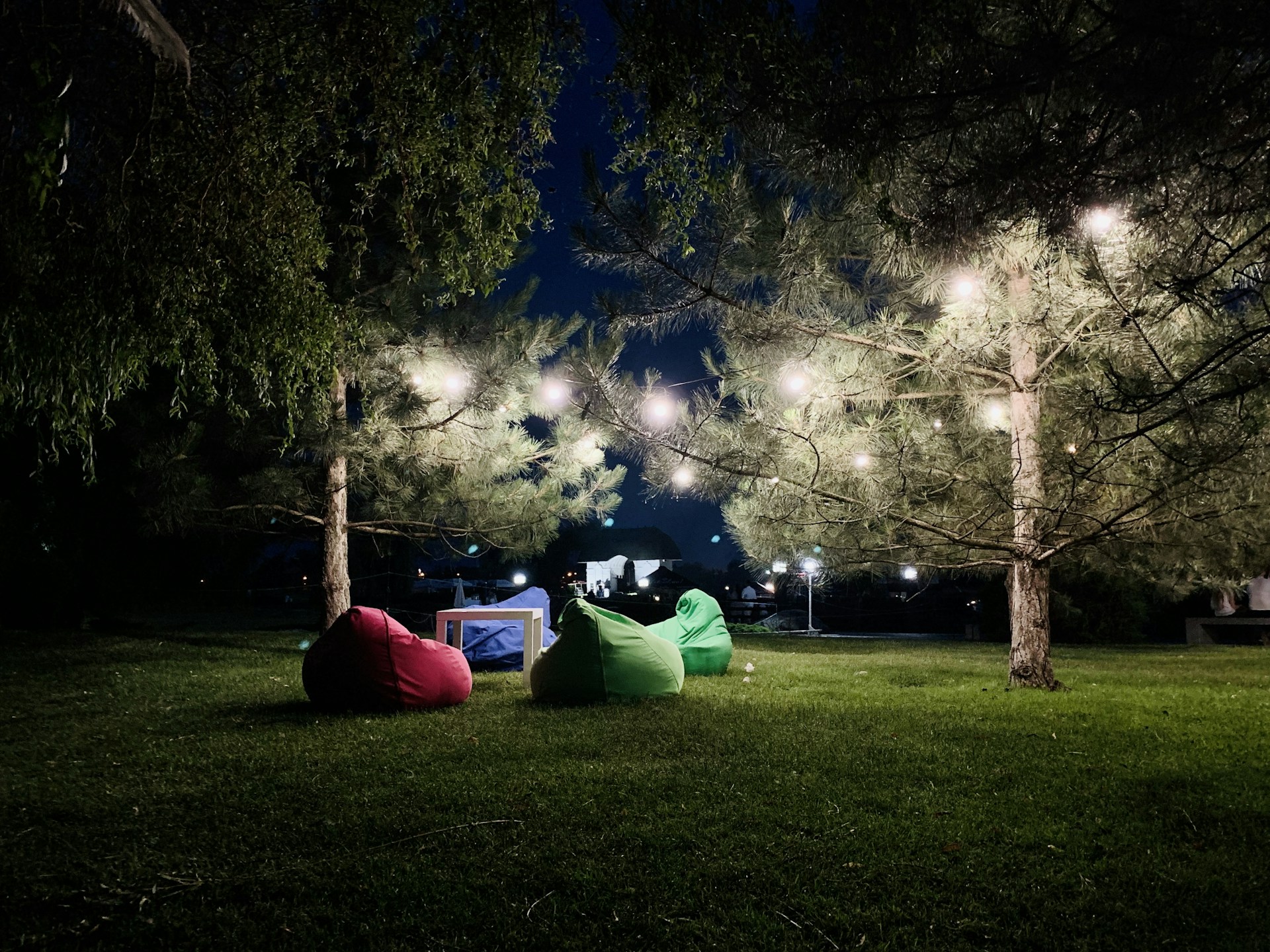 A cozy backyard setup with a large outdoor screen, comfy bean bags, and string lights glowing warmly as families settle in for a movie night.