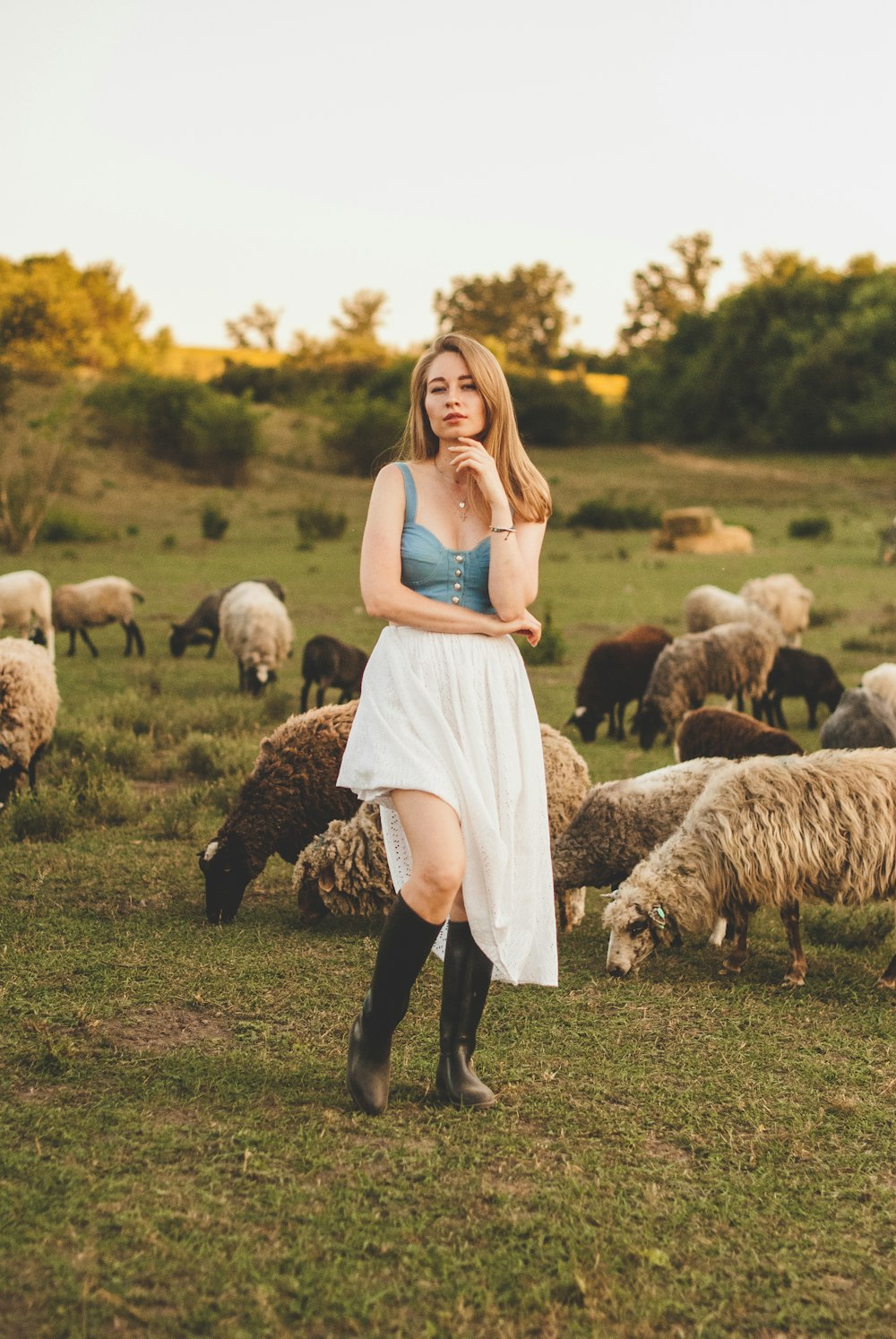 woman in blue tank top standing on green grass field with sheep during daytime