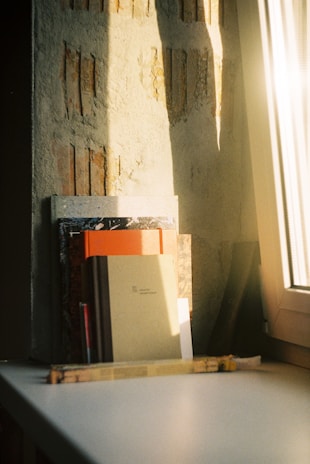 Stack of textbooks and stationery items with a bright sunny window in the background