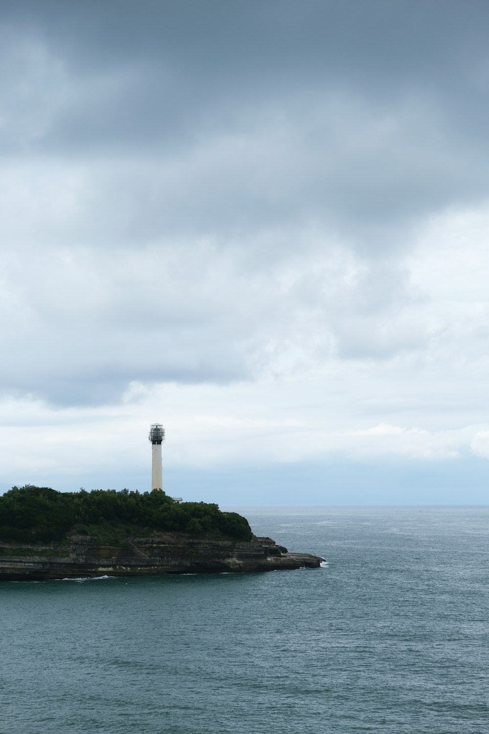 white lighthouse on top of green island surrounded by body of water under white clouds during