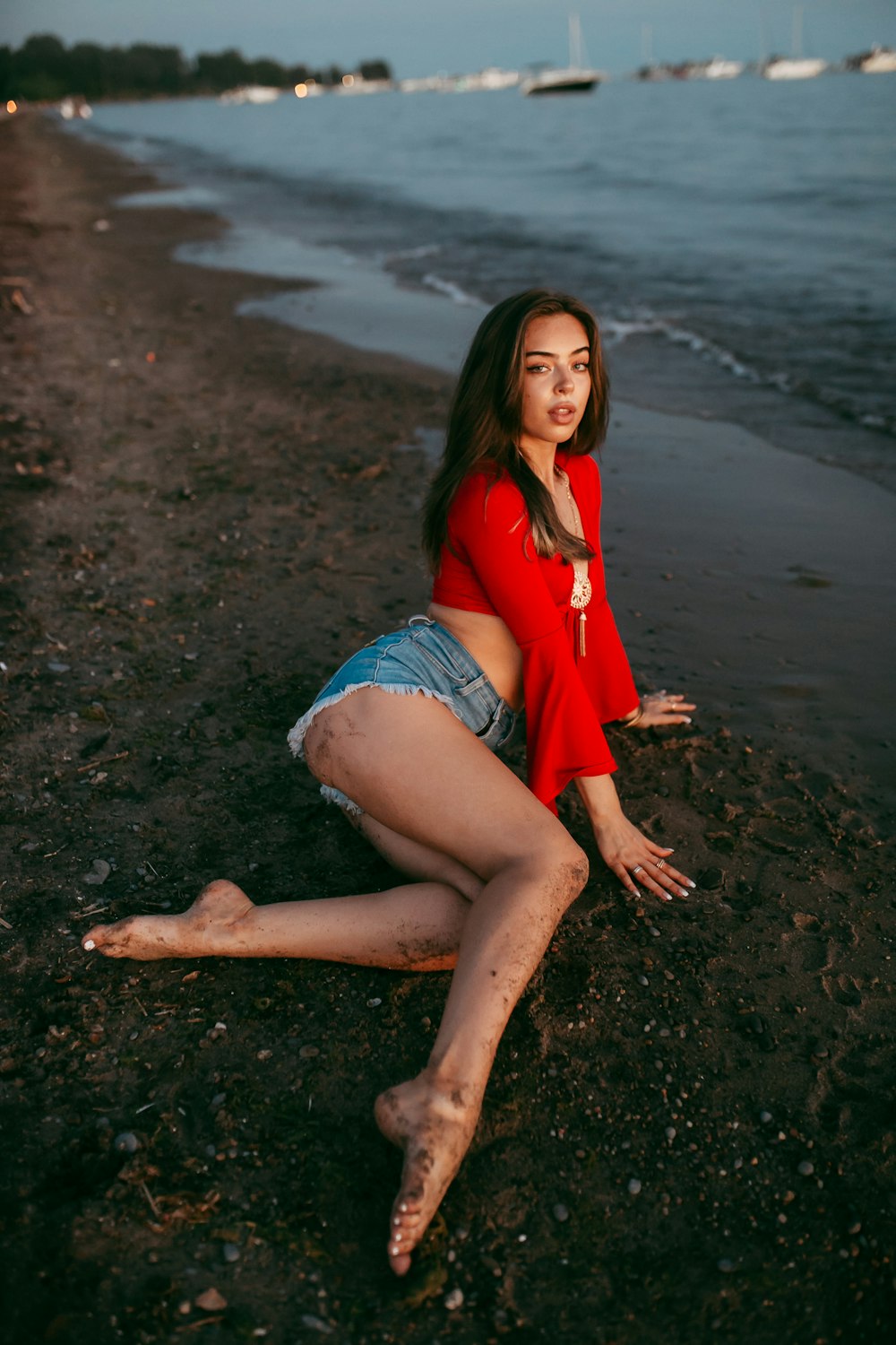 Woman in red shirt and blue denim shorts sitting on brown sand
