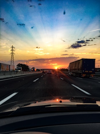 A convoy of light motor vehicles being transported on a highway at sunset.