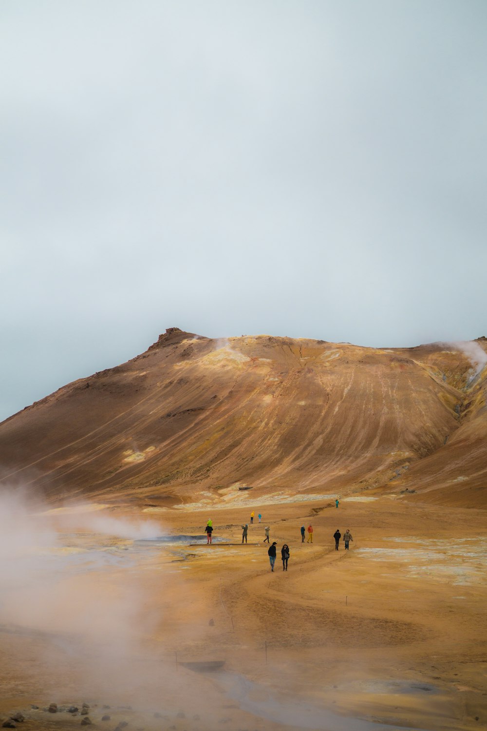 people walking on brown field near brown mountain under white clouds during daytime