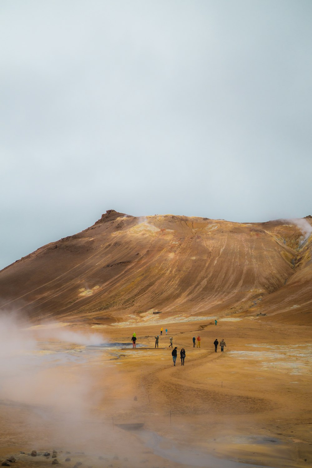 Persone che camminano sul campo marrone vicino alla montagna marrone sotto le nuvole bianche durante il giorno