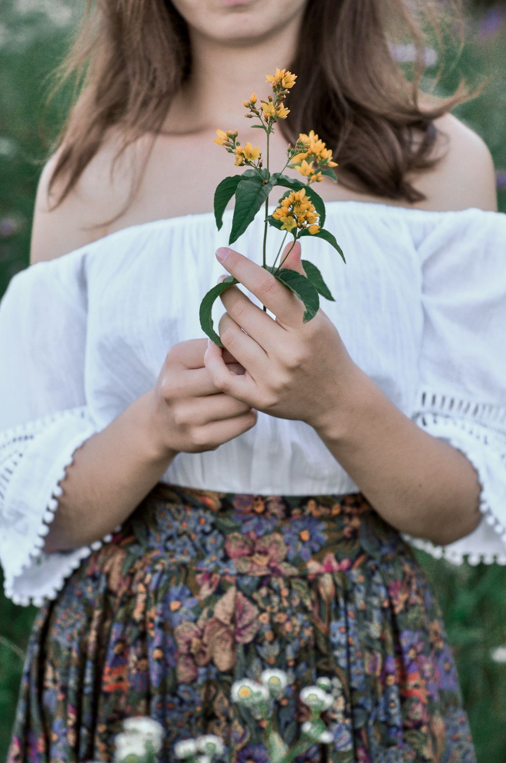 mujer en vestido floral blanco sosteniendo flor amarilla