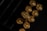 A close-up view of gold-colored bullet casings arranged in a box, with the headstamp reading '9mm Luger' visibly engraved on one of the casings. The lighting creates a reflective and metallic sheen on the surfaces.