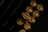 A close-up view of gold-colored bullet casings arranged in a box, with the headstamp reading '9mm Luger' visibly engraved on one of the casings. The lighting creates a reflective and metallic sheen on the surfaces.