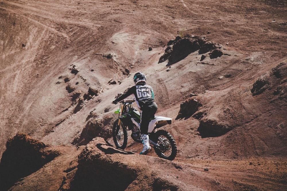 Hombre con chaqueta blanca y negra montando motocross en una montaña rocosa marrón durante el día
