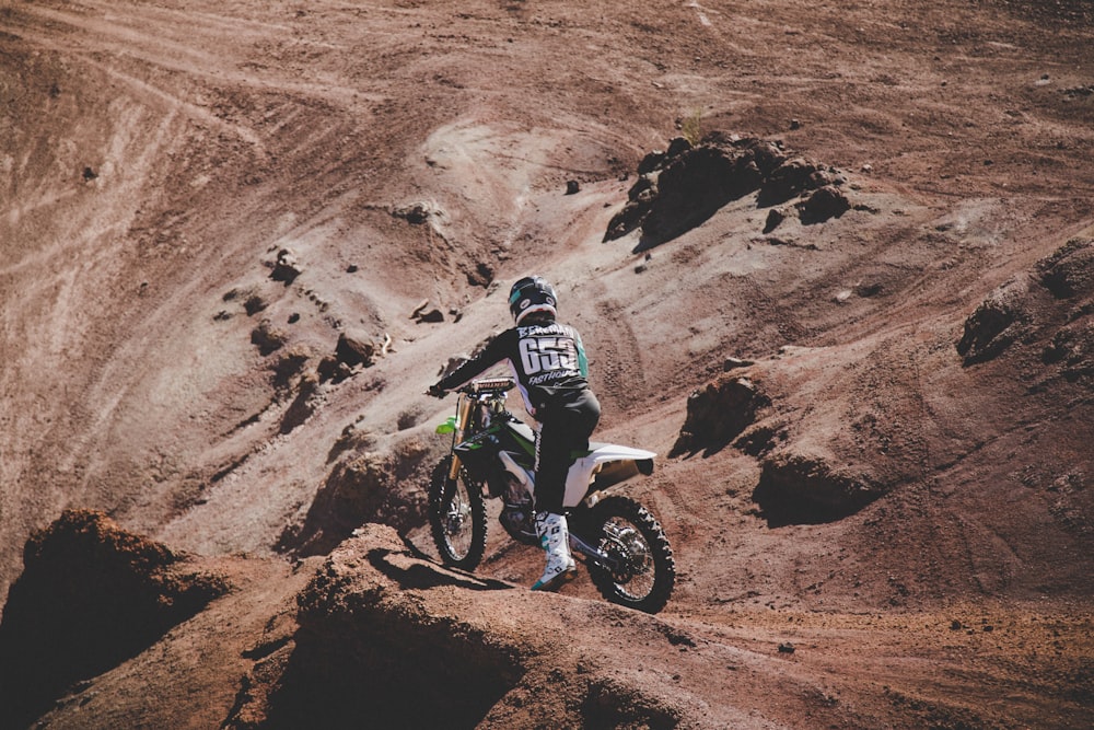 man in black and white jacket riding motocross dirt bike on brown rocky mountain during daytime