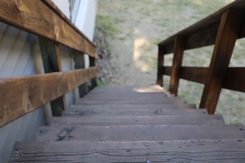 Wooden stairs with handrails descend into a grassy area. The focus is on the textured wood, showing natural grain and some wear.