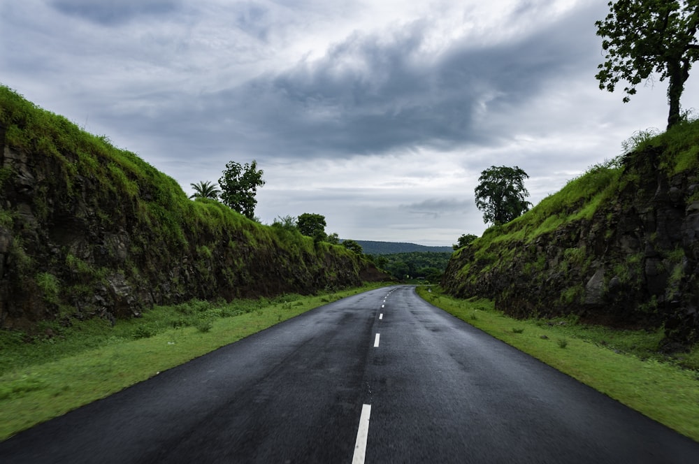 gray concrete road between green grass field under white clouds during daytime