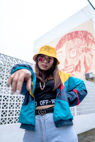 A colorful bucket hat with playful graffiti-style prints, hanging against a brick wall with peeling paint.