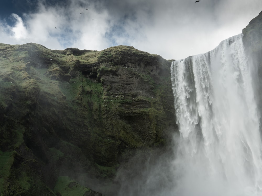 waterfalls on green and brown mountain under white clouds during daytime