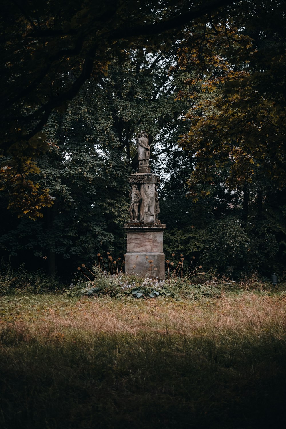 Statue en béton brun entourée d’arbres verts pendant la journée