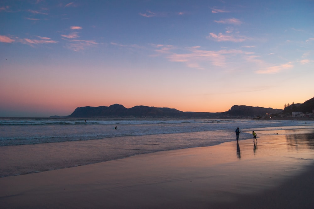 silhouette of 2 people walking on beach during sunset