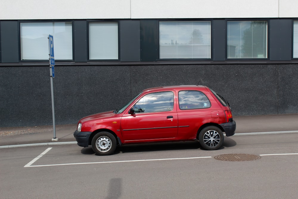 Hatchback rojo de 5 puertas estacionado junto a un edificio de concreto gris durante el día
