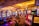A vibrant casino interior filled with rows of colorful slot machines, each illuminated with bright lights and displays. The ceiling is adorned with elegant chandeliers and golden drapes, creating a luxurious atmosphere. The patterned carpet adds to the elaborate design of the space.