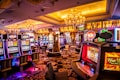 A vibrant casino interior filled with rows of colorful slot machines, each illuminated with bright lights and displays. The ceiling is adorned with elegant chandeliers and golden drapes, creating a luxurious atmosphere. The patterned carpet adds to the elaborate design of the space.