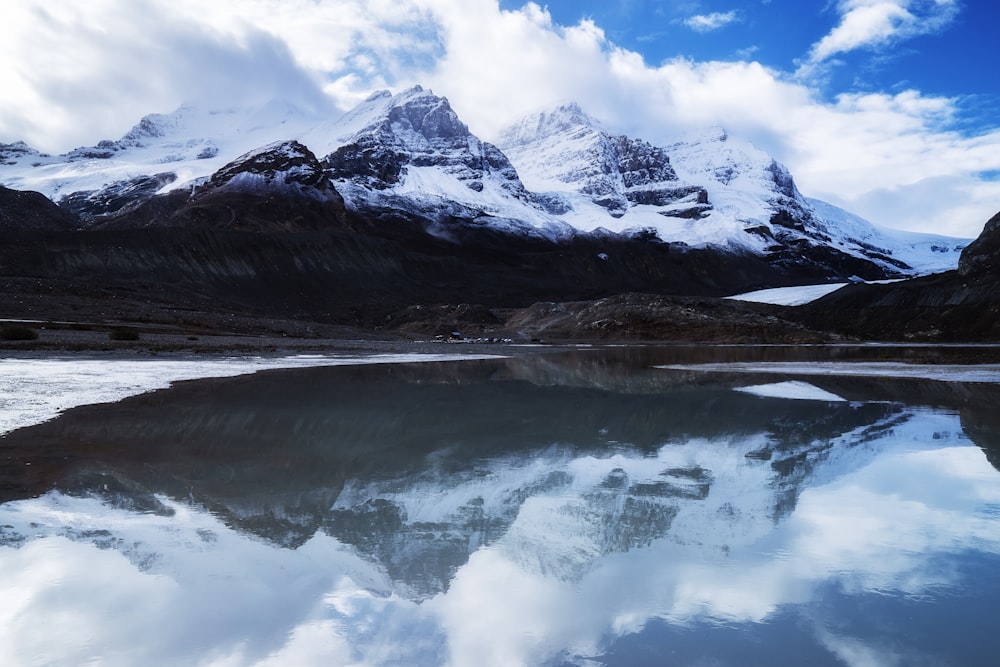 snow covered mountain near lake under cloudy sky during daytime