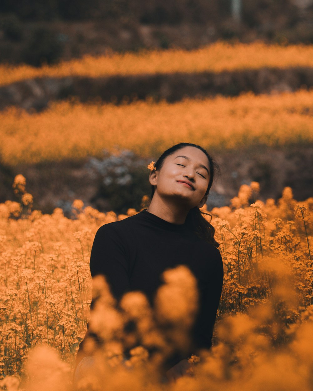 woman in black turtleneck shirt standing on yellow flower field during daytime