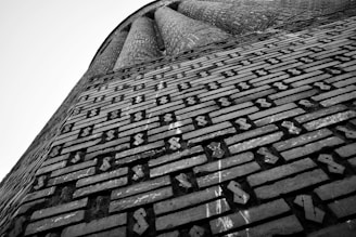 An architectural structure with intricate brickwork, featuring a geometric pattern. The bricks are arranged in a regular and repetitive design, with diagonal and vertical lines creating a visually striking texture. The perspective is angled upwards, giving a sense of height and grandeur.