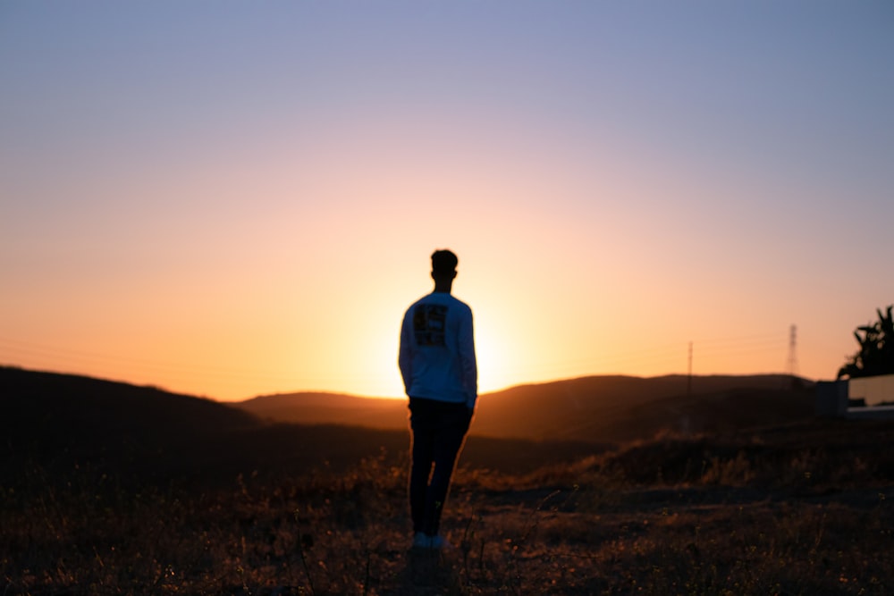 Mann im blauen Hemd steht bei Sonnenuntergang auf brauner Wiese