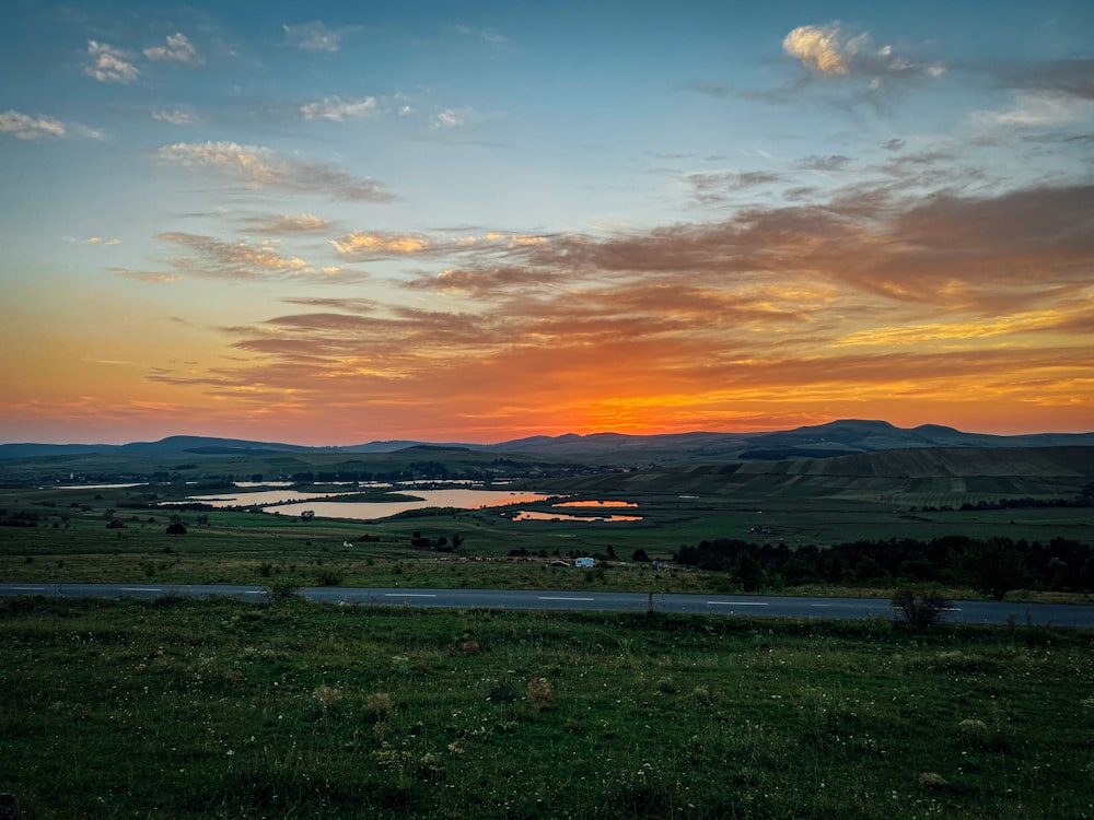 green grass field near body of water during sunset