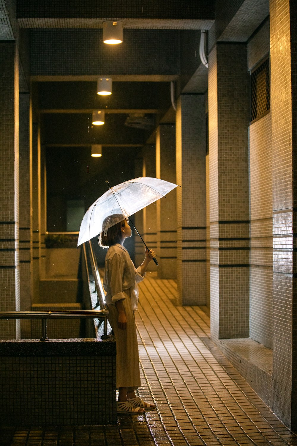 Femme en manteau marron tenant un parapluie marchant sur le trottoir pendant la journée