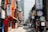 A bustling urban street in a city lined with numerous colorful signs in Korean, indicating shops, restaurants, and coffee shops. The street has a mix of modern and traditional signage, with pedestrians and vehicles moving through. Tall buildings flank both sides of the street.