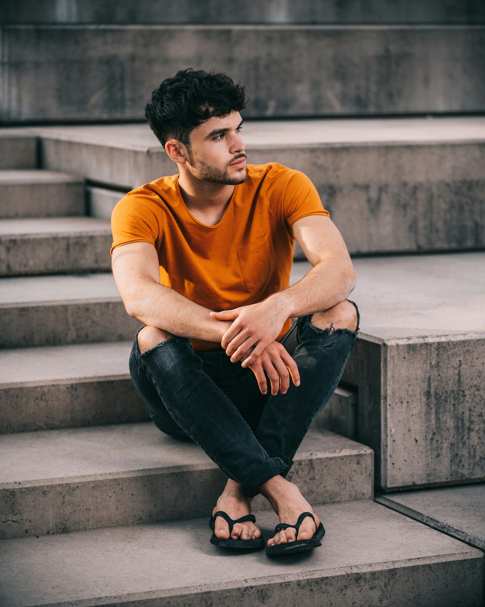 man in yellow crew neck t-shirt and black denim jeans sitting on concrete stairs