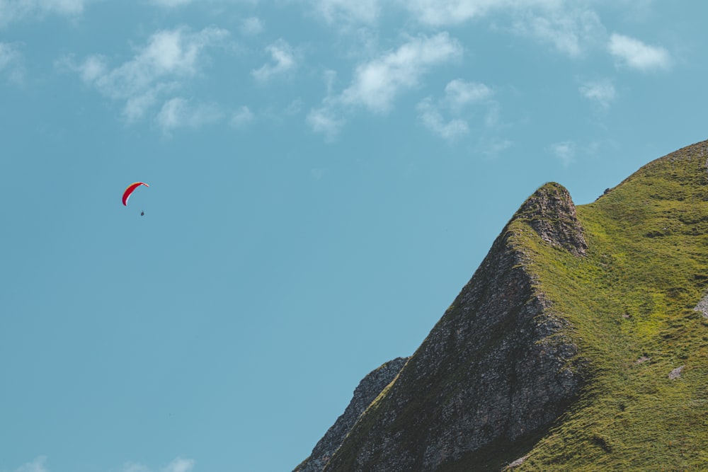 person in orange parachute over green mountain during daytime