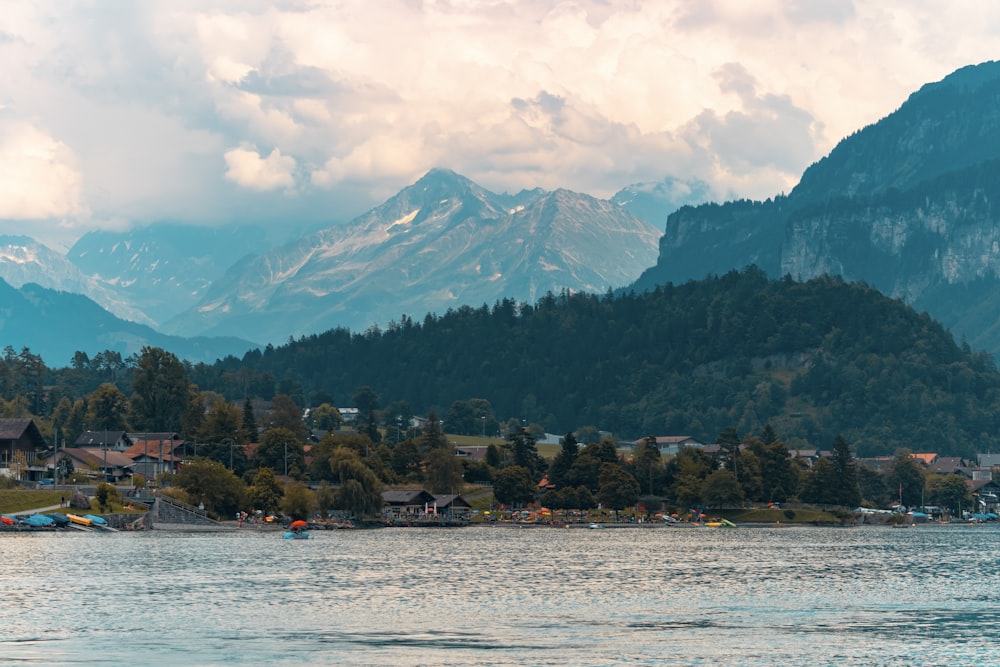 green trees near body of water and mountain under white clouds and blue sky during daytime