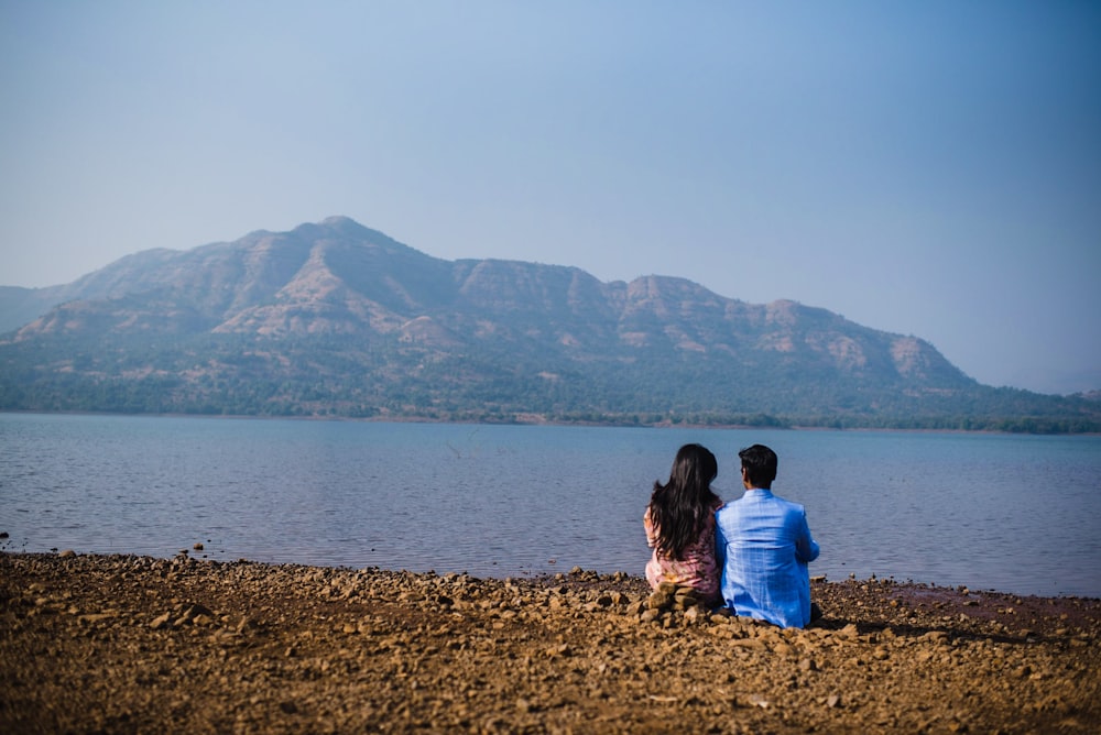 woman in blue shirt sitting on brown sand near body of water during daytime