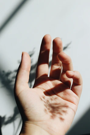 Close-up of hands gently stretching with soft natural light and leafy shadows.