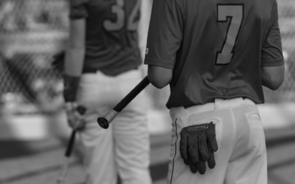 grayscale photo of man in black crew neck t-shirt and white pants holding baseball bat