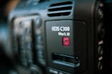 Close-up of a professional video camera, showcasing the EOS C300 Mark III model insignia. The focus is on the branding, with partial views of buttons and controls in the blurred background.