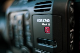 Close-up of a professional video camera, showcasing the EOS C300 Mark III model insignia. The focus is on the branding, with partial views of buttons and controls in the blurred background.